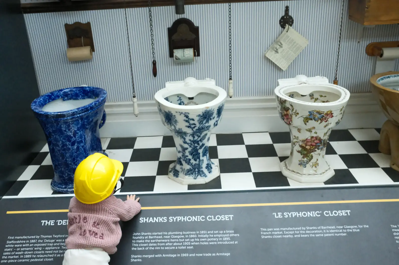Toddler in a yellow hard hat looking at historic toilets in the Toilet Timeline exhibition. Photo: Diana Kostino
